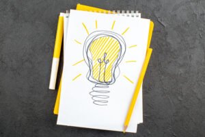 top-view-yellow-idealight-bulb-drawing-notepad-marker-pencil-black